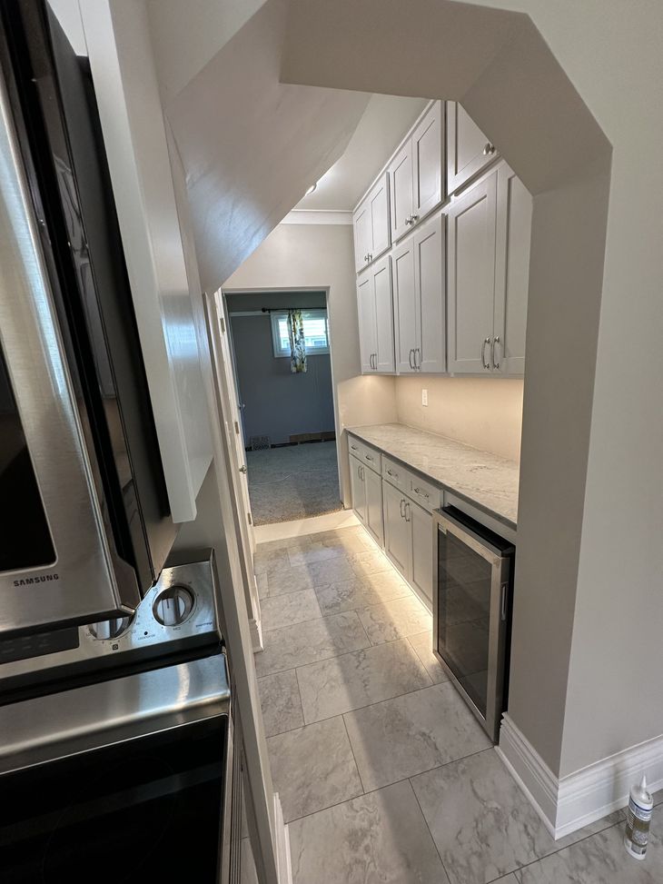 Gray cabinets with white countertops, under-cabinet lighting, and a wine cooler in a kitchen.