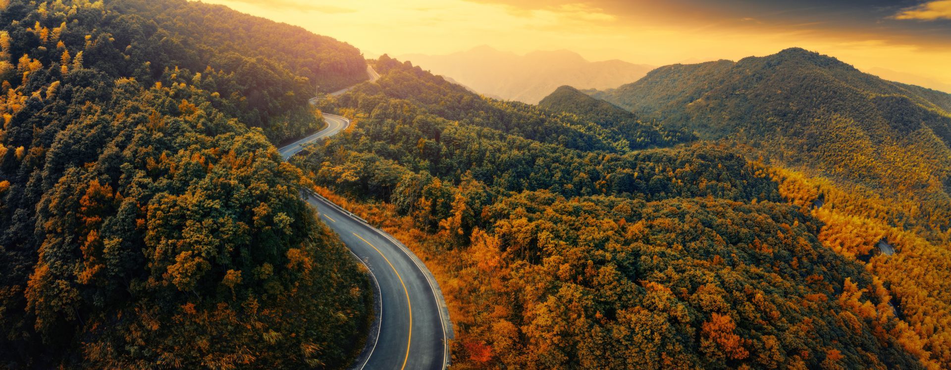 An aerial view of a winding road through a forest at sunset.