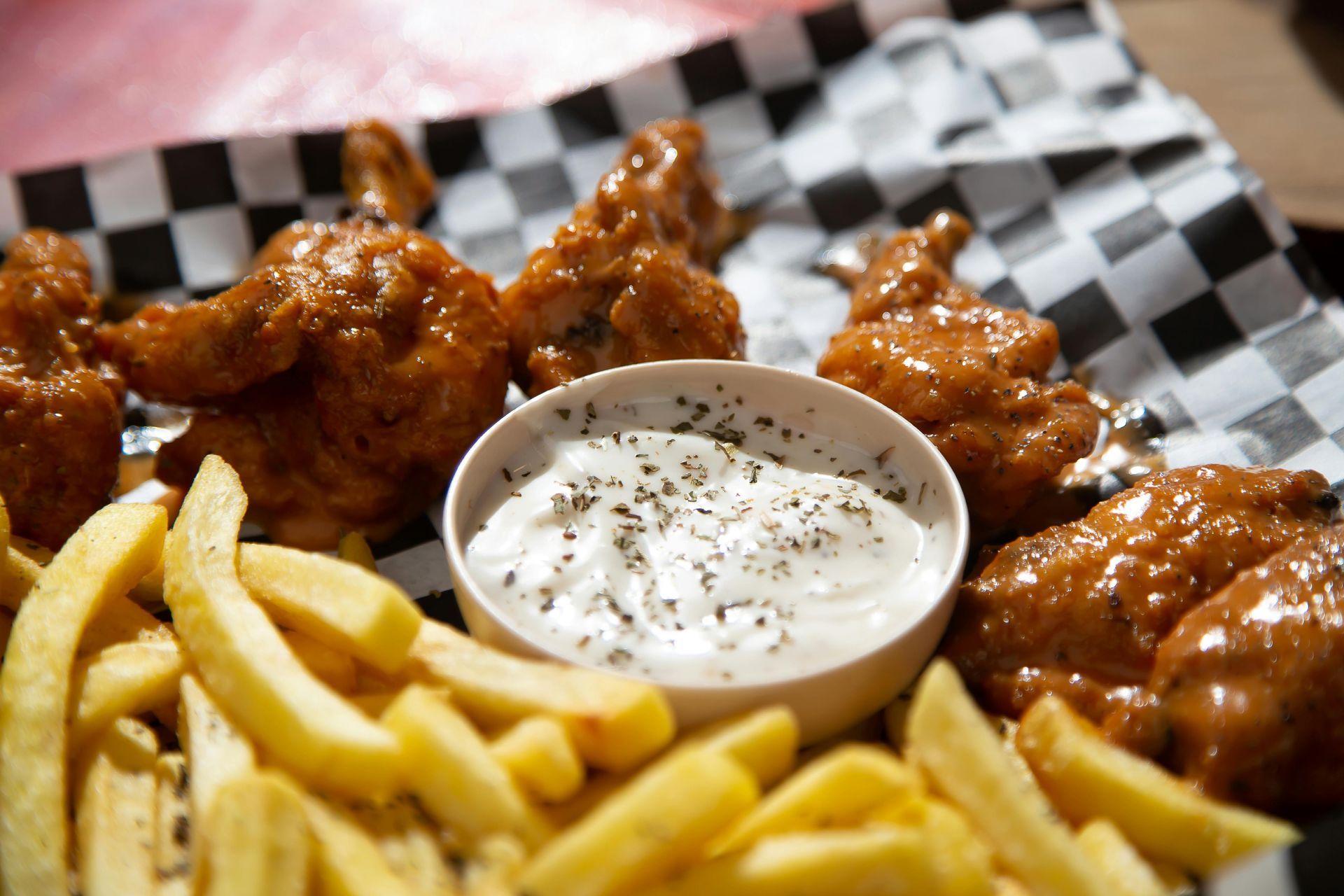 Buffalo wings, fries, and dipping sauce on a checkered paper-lined tray.