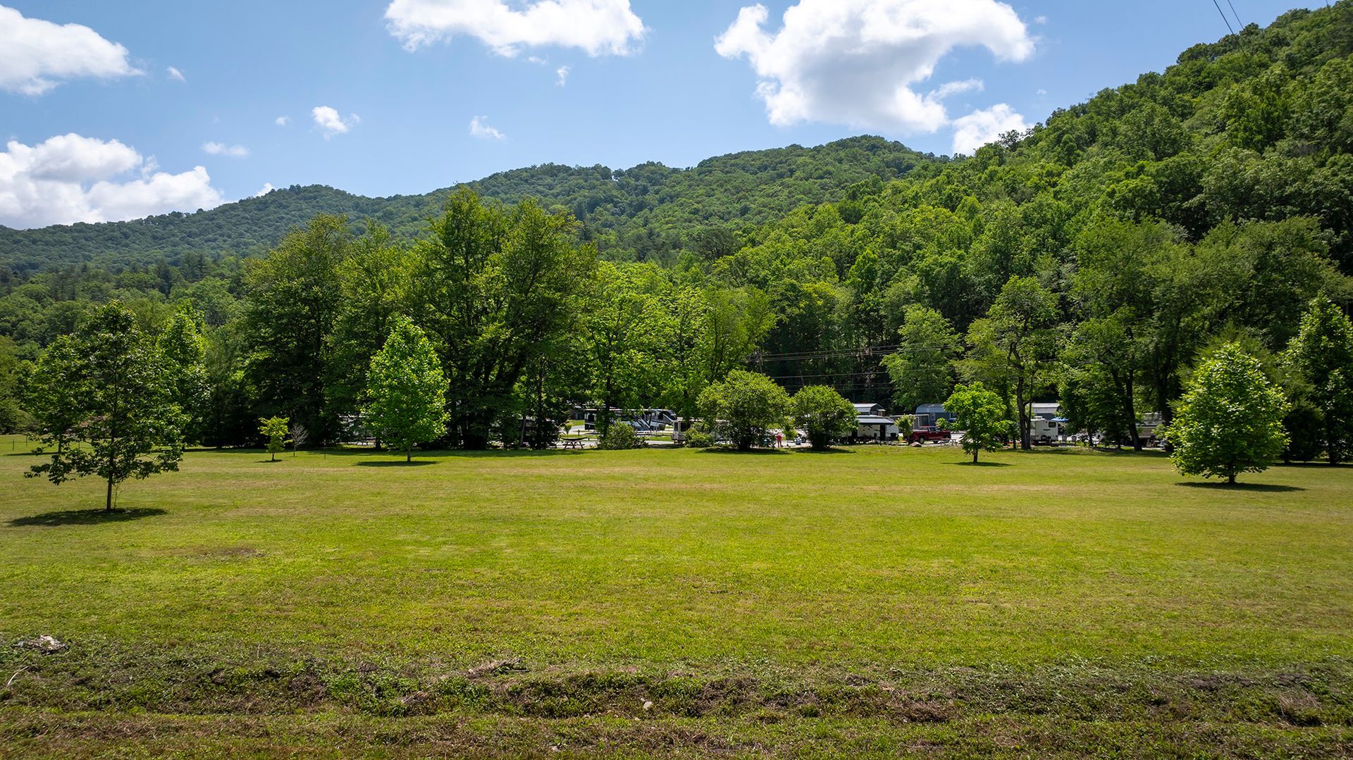 Green field with trees in front of a lush mountain backdrop. Campers and RVs are parked in the trees.