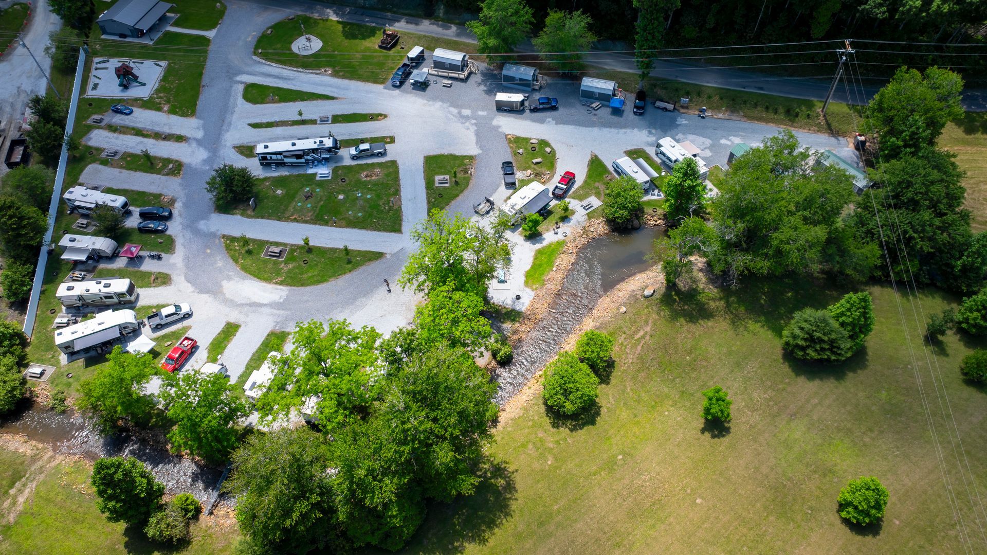 Aerial view of a campsite with RVs parked on gravel pads near trees and a creek.