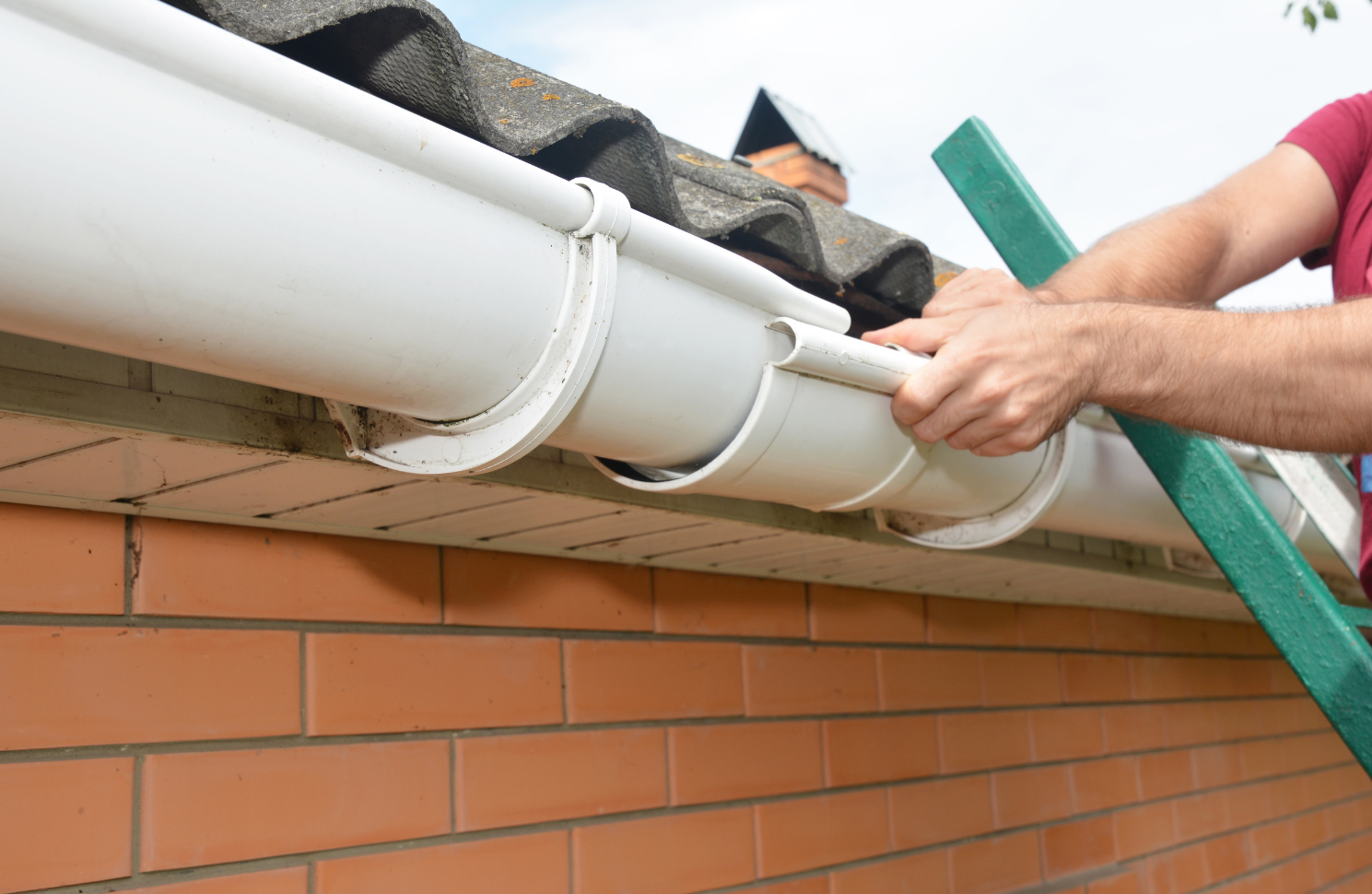 A man is using a ladder to install a gutter on the roof of a house.
