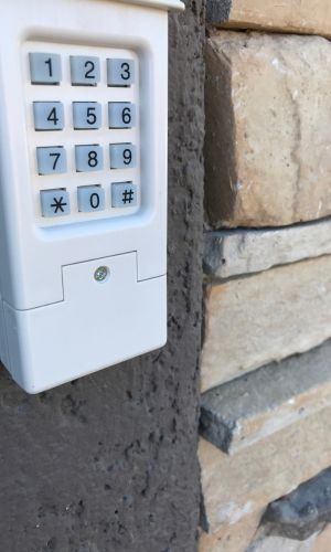 A white keypad is attached to a brick wall.