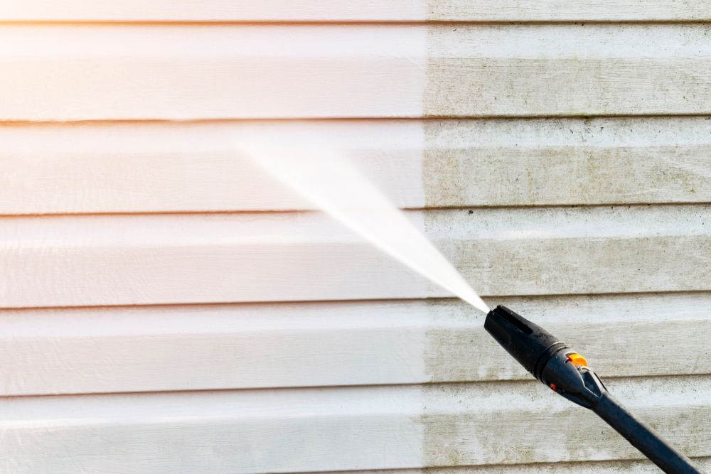A person is cleaning the side of a house with a high pressure washer.