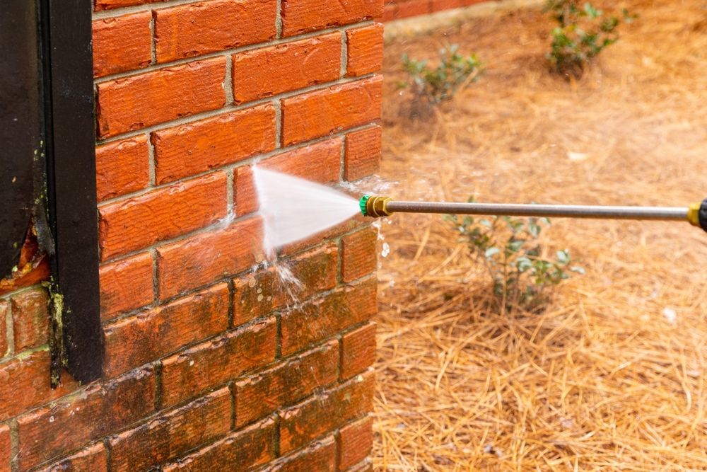 A person is cleaning a brick wall with a high pressure washer.