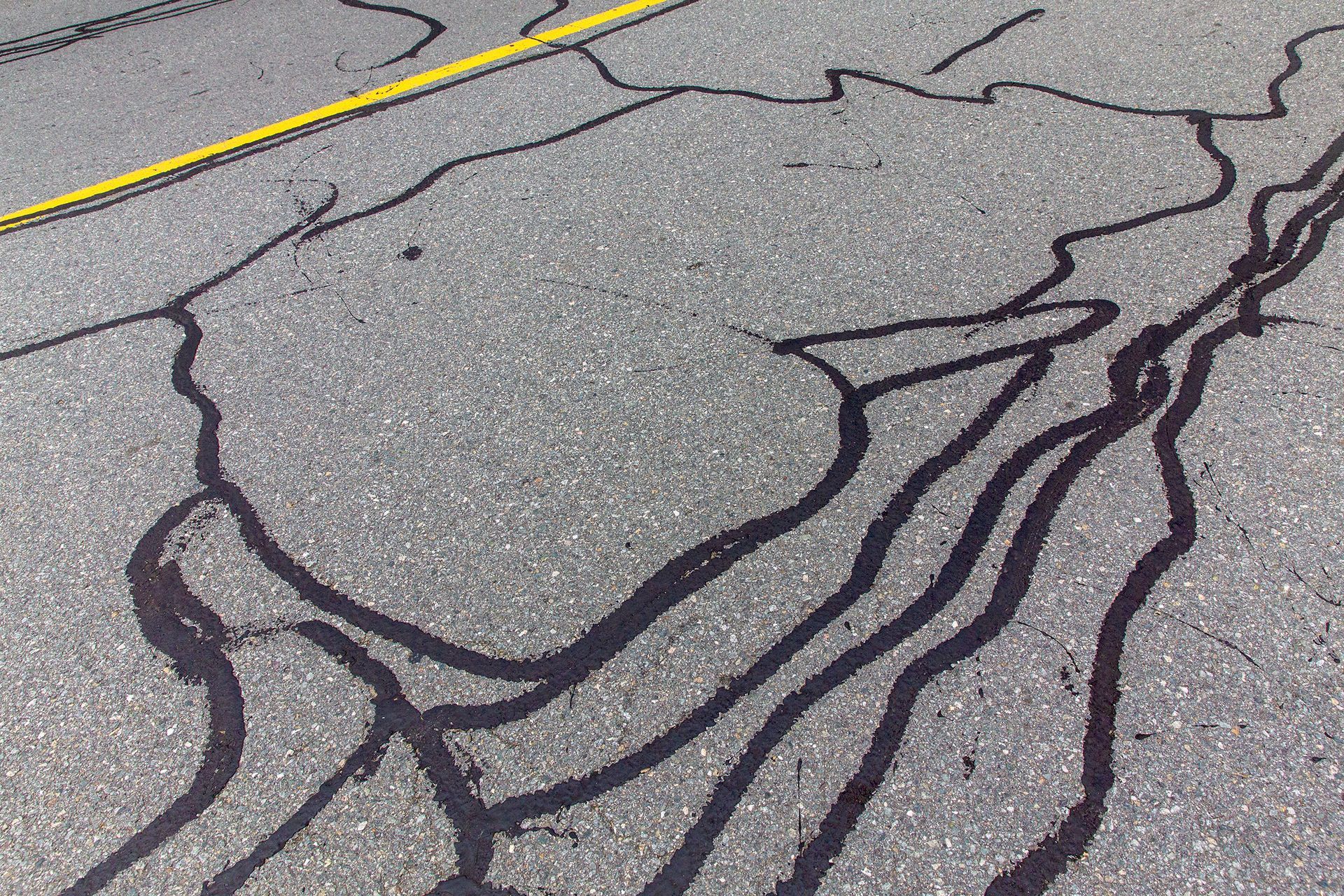 Asphalt pavement with dark sealant filling cracks. Yellow line present in the upper left corner.