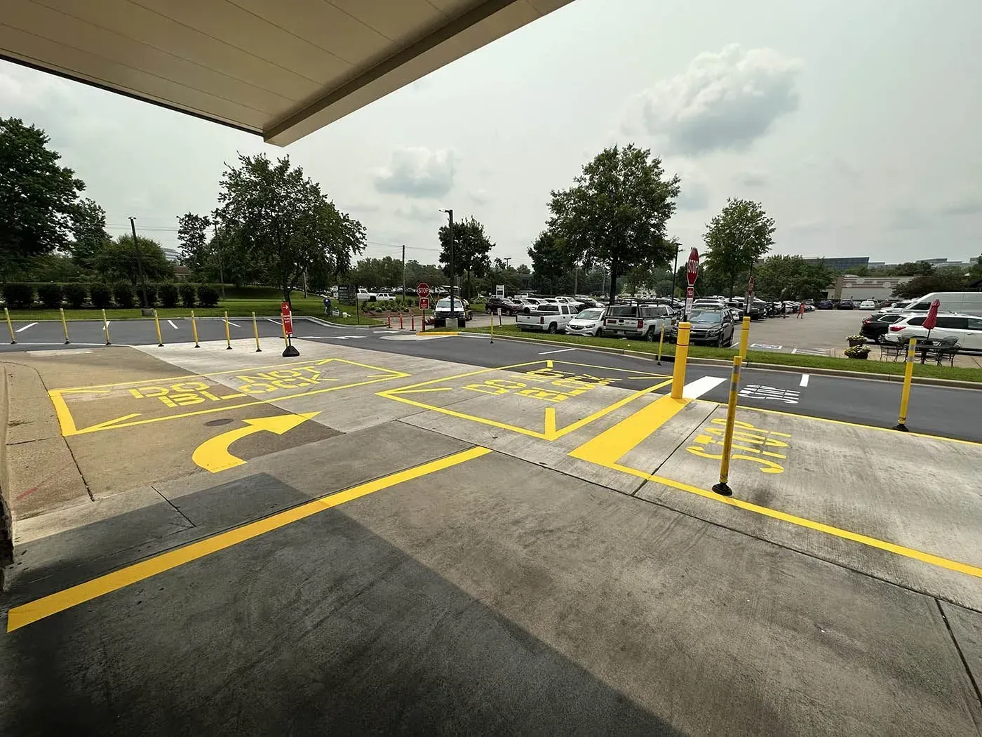 A view of a parking lot entrance with yellow painted arrows and markings on the pavement. A canopy shades the foreground.