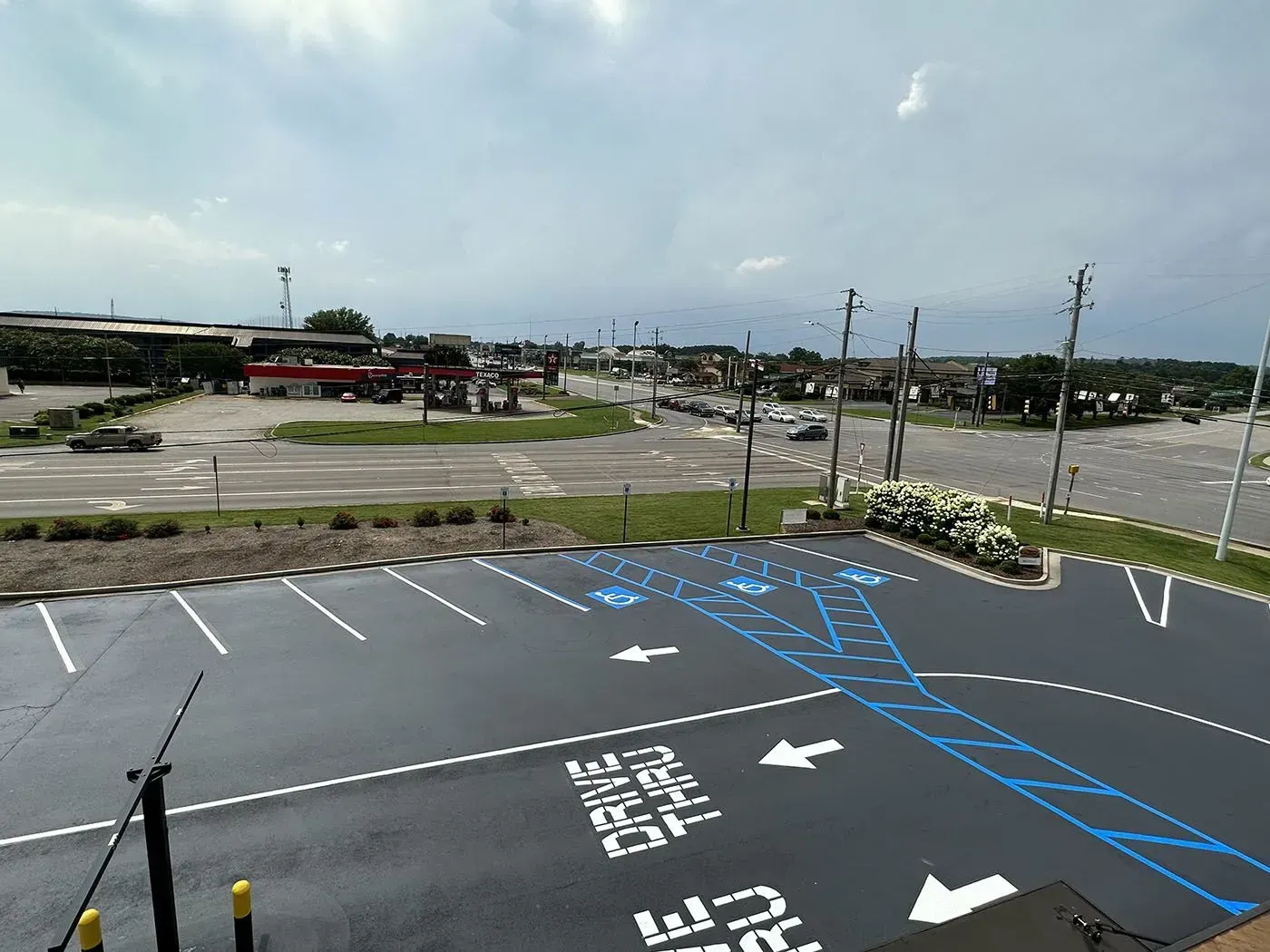Overhead view of a parking lot with drive-thru lanes, leading towards a street with businesses under a cloudy sky.
