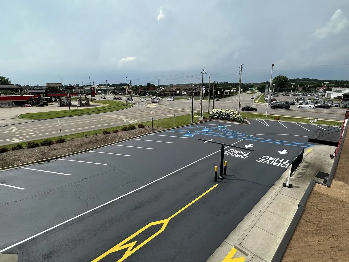 An overhead view of a black asphalt parking lot with yellow lane markings and painted directional arrows.