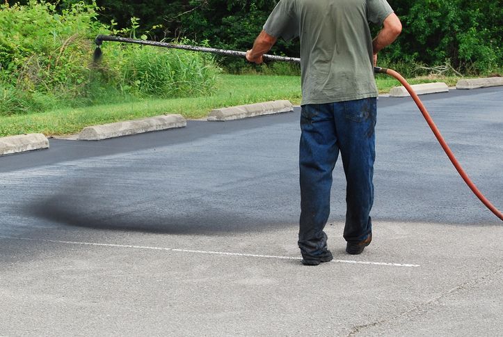 Person sealing asphalt in parking lot with long hose.