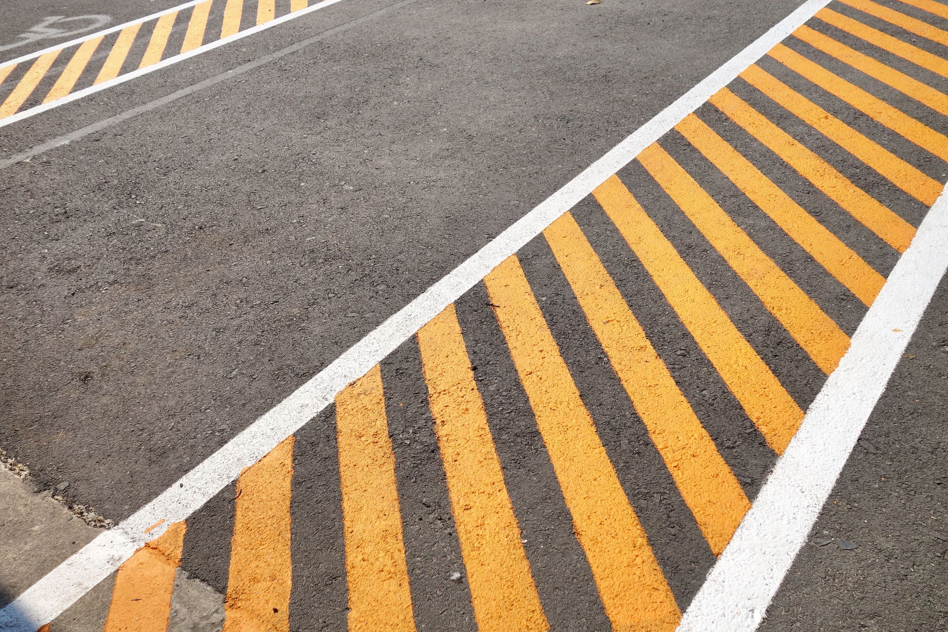 Yellow diagonal stripes inside a white border on asphalt pavement, likely a marked parking or loading zone.