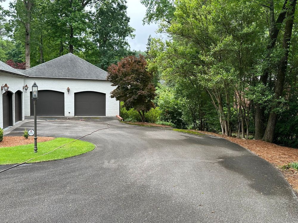 Asphalt driveway leading to a white garage with dark brown doors. Trees line the right side.