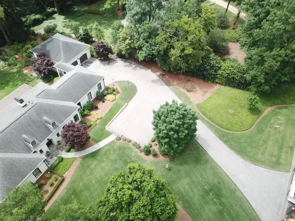 Aerial view of a large house with a gray roof, surrounded by a circular driveway and lush greenery.
