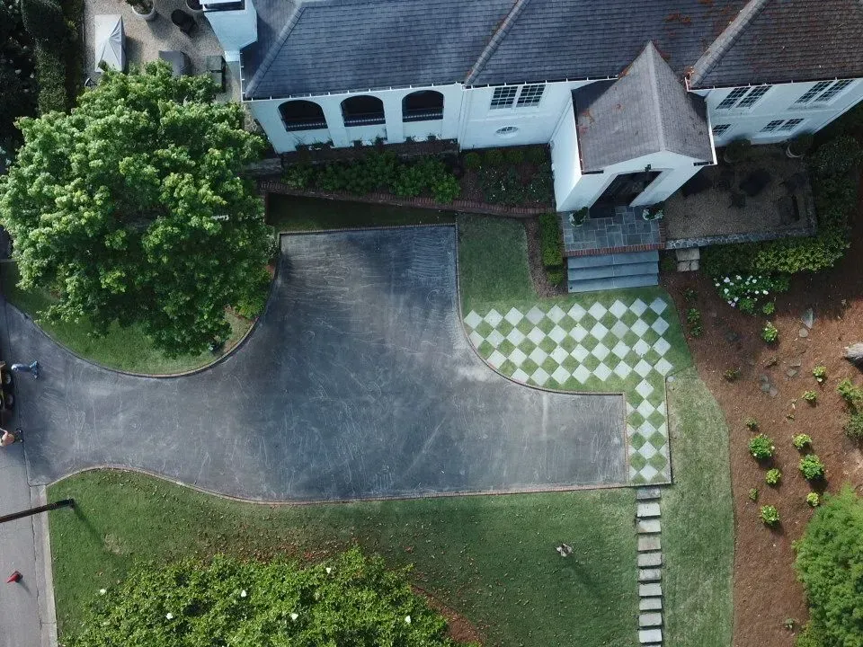 Overhead view of a house with a driveway, checkered walkway, and surrounding greenery.