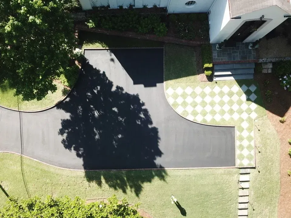 Overhead view of a house with a black asphalt driveway curving around a tree, and a green and white checkered walkway.