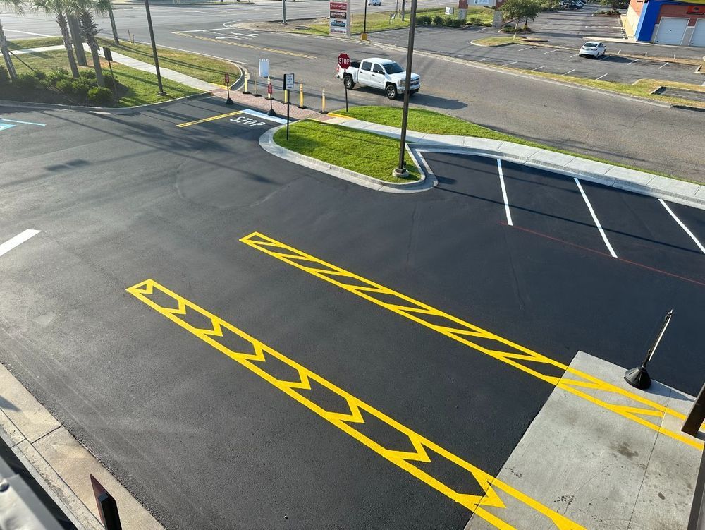 Freshly paved parking lot with yellow directional arrows, a white pickup truck, and a building in the background.