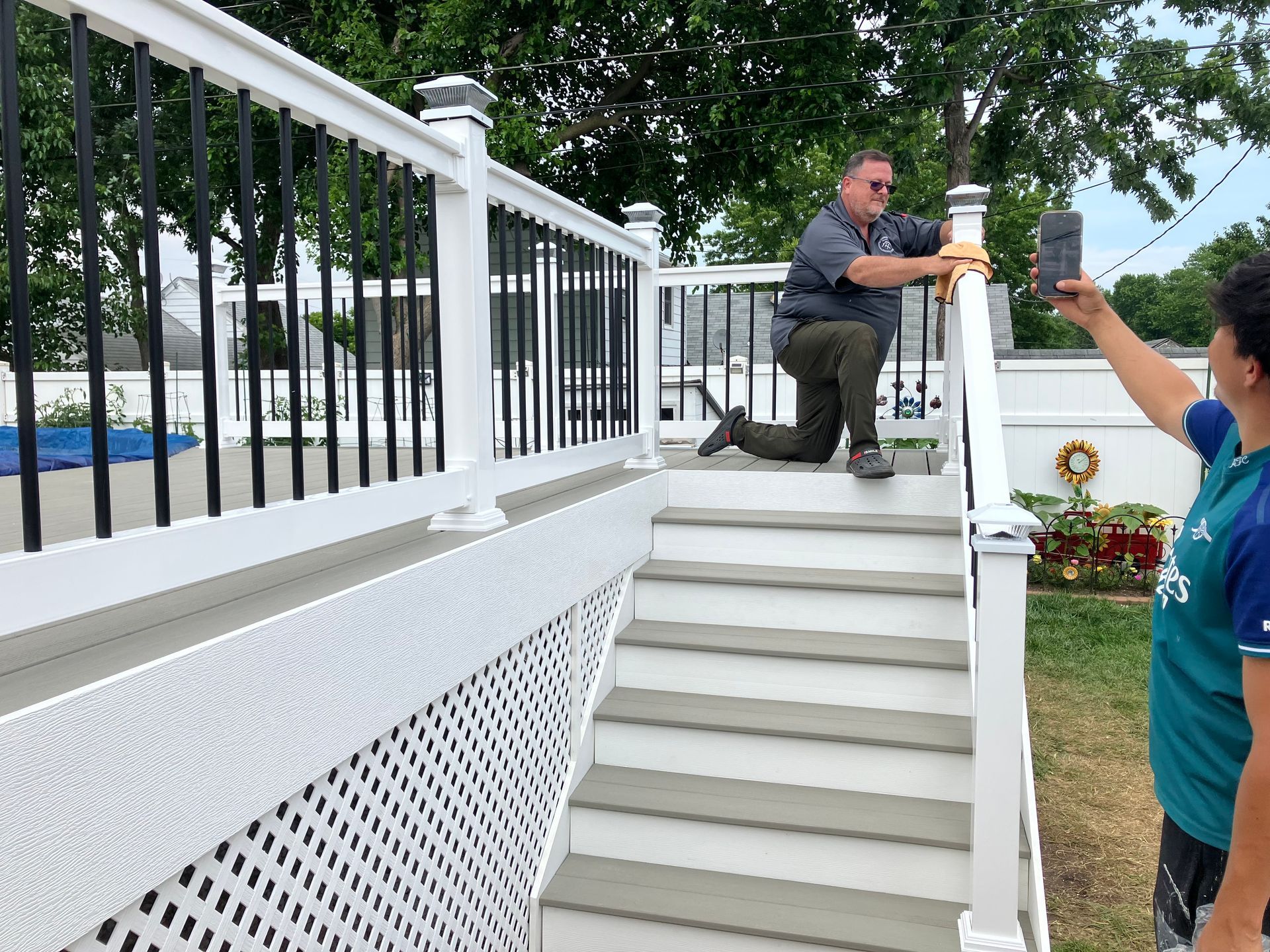 A man is kneeling down on a deck while a boy takes a picture of him.