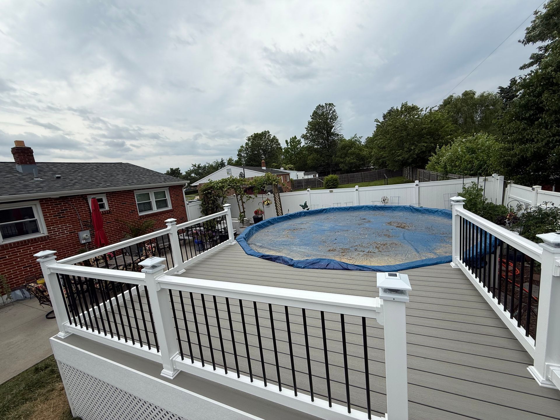 A deck with a swimming pool in the background and a house in the background.