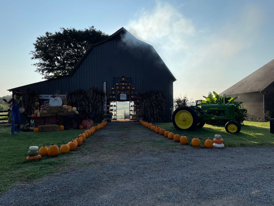 A tractor is parked in front of a barn decorated with pumpkins.