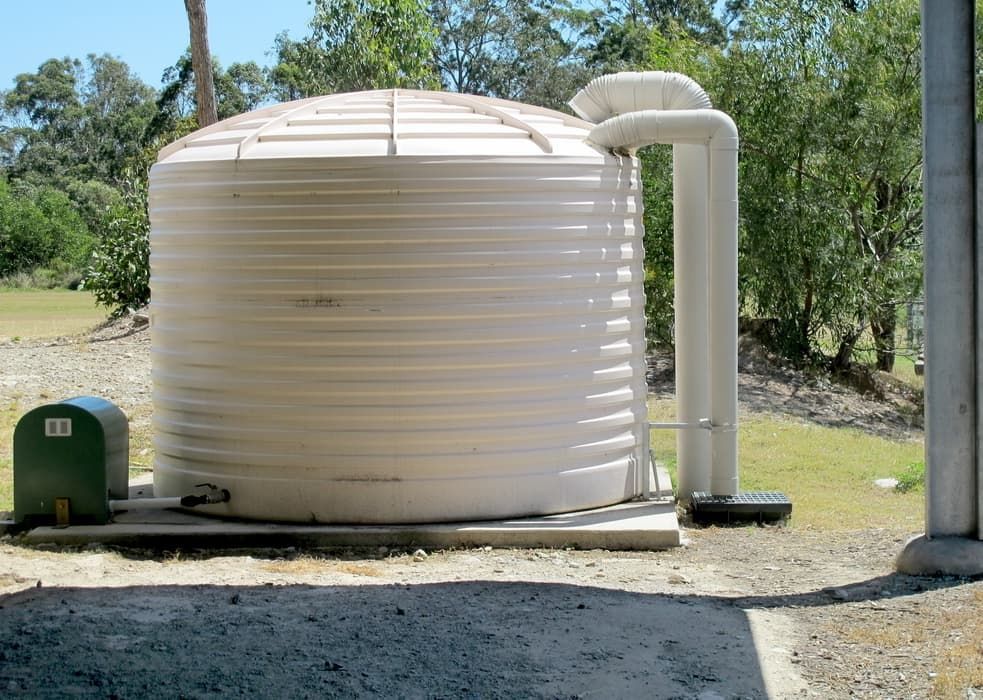 A Large White Water Tank Is Sitting In A Grassy Field — Flavell Plumbing (NT) Pty Ltd In Ciccone, NT