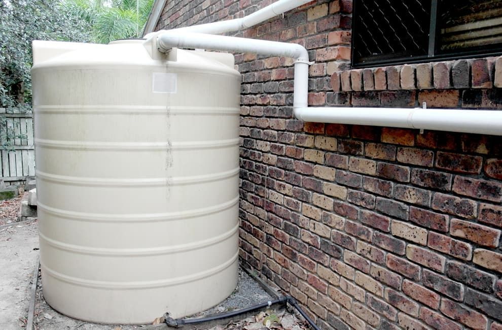 A Large White Water Tank Is Attached To The Side Of A Brick Building — Flavell Plumbing (NT) Pty Ltd In Ciccone, NT