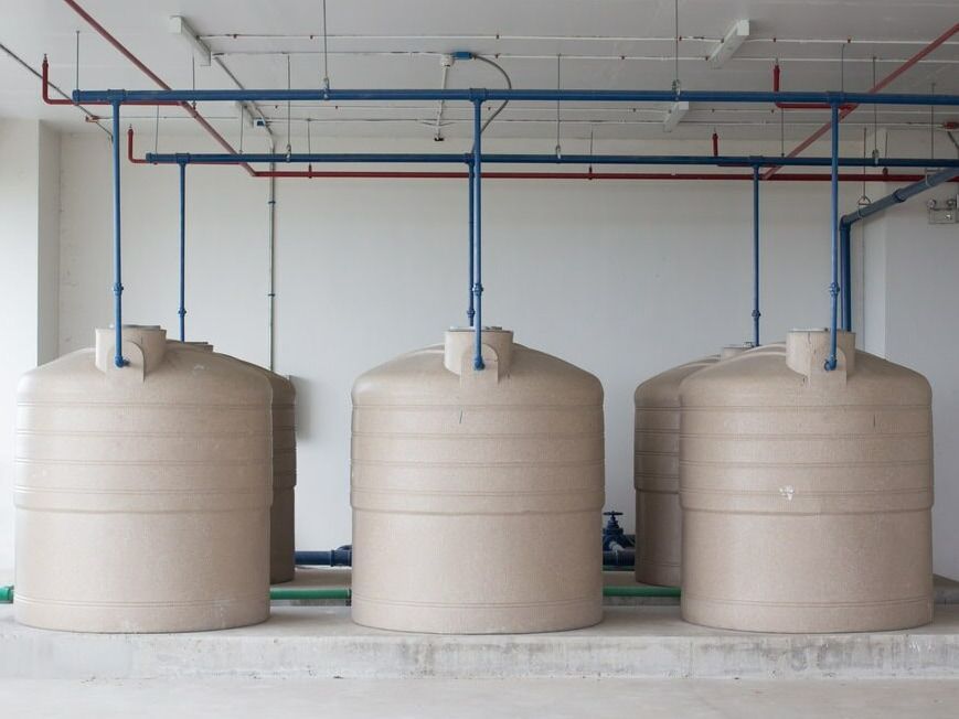Three Large Tanks Are Lined Up In A Room With Pipes Hanging From The Ceiling — Flavell Plumbing (NT) Pty Ltd In Ciccone, NT