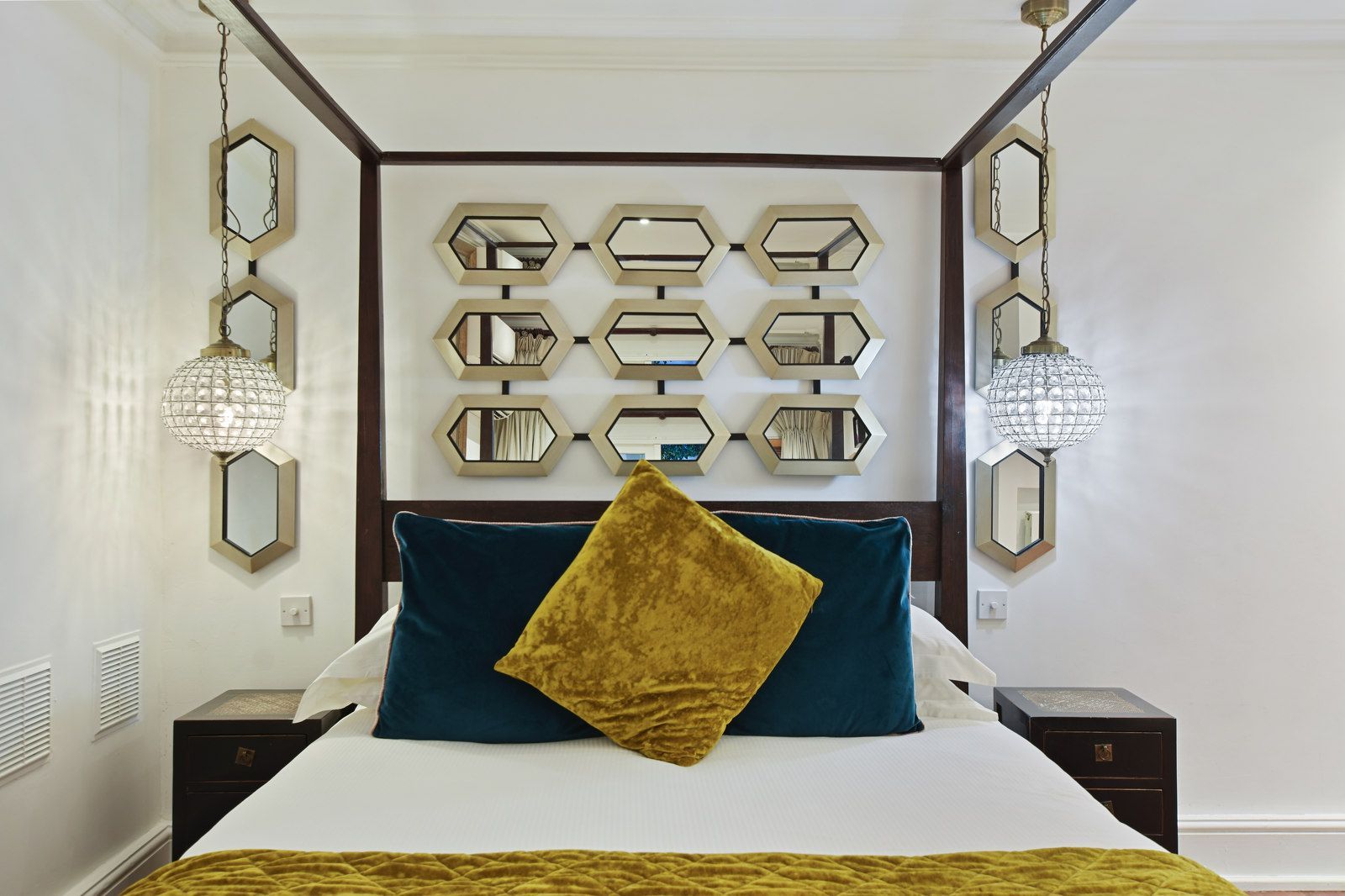 Bedroom with canopy bed, decorated with mirrors, hanging lights, and velvet pillows in teal and gold.