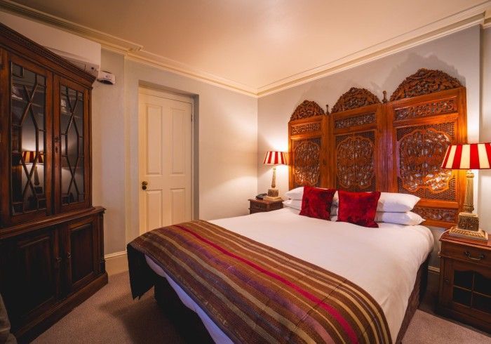 Bedroom with carved wooden headboard, red pillows, striped blanket, and antique cabinet.