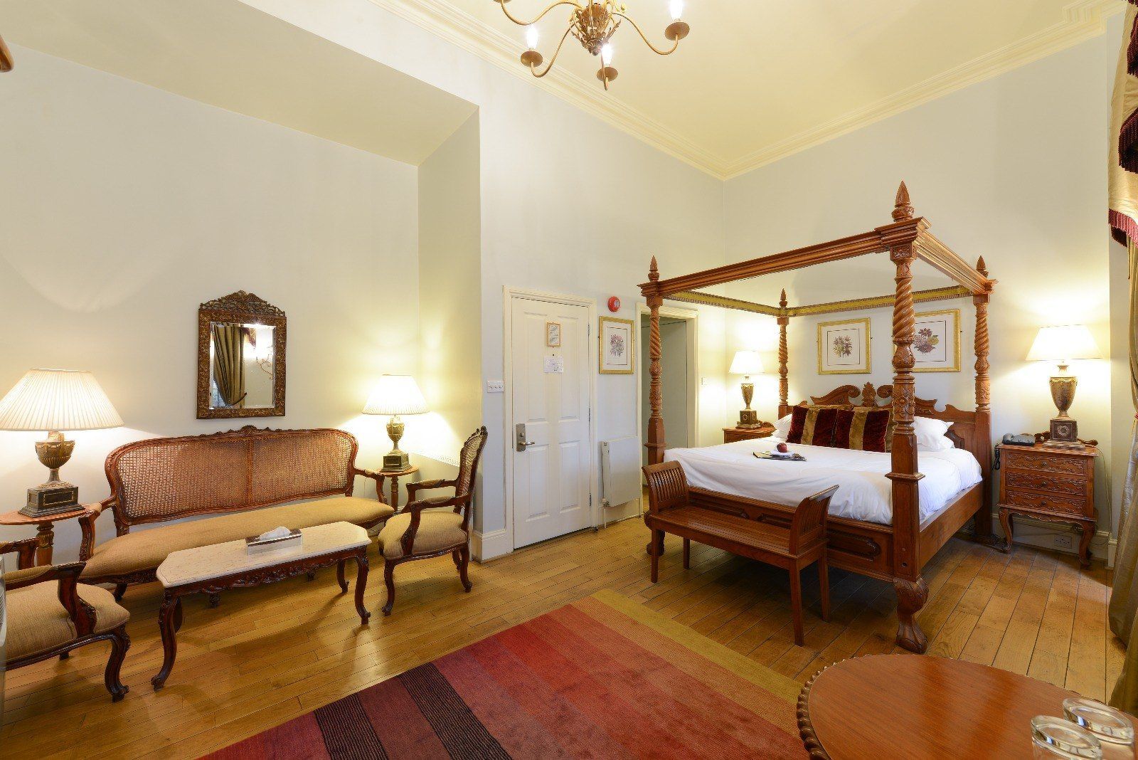 Luxurious hotel room with four-poster bed, sitting area, and oriental rug.