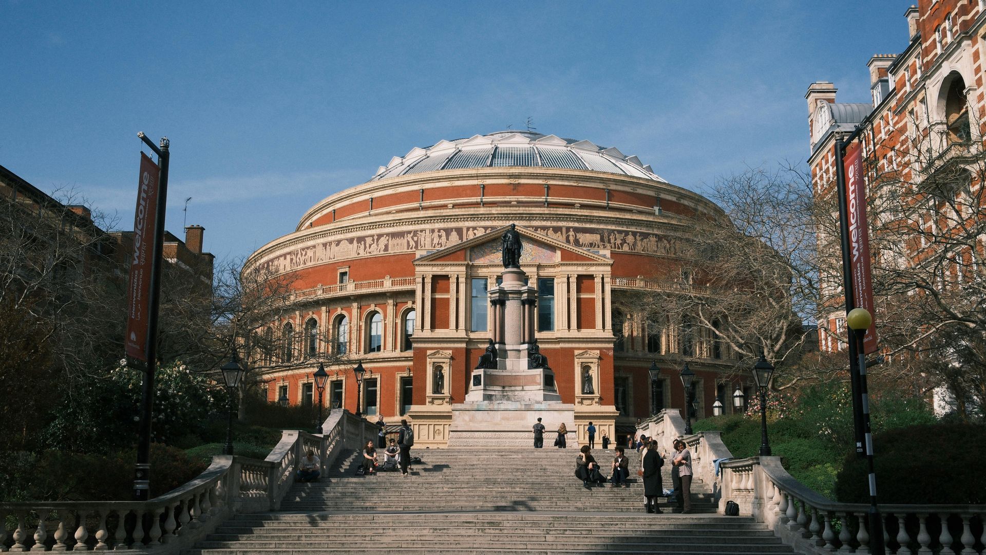 Royal Albert Hall, with a central staircase leading up to the entrance. The building is brick with a large glass dome.