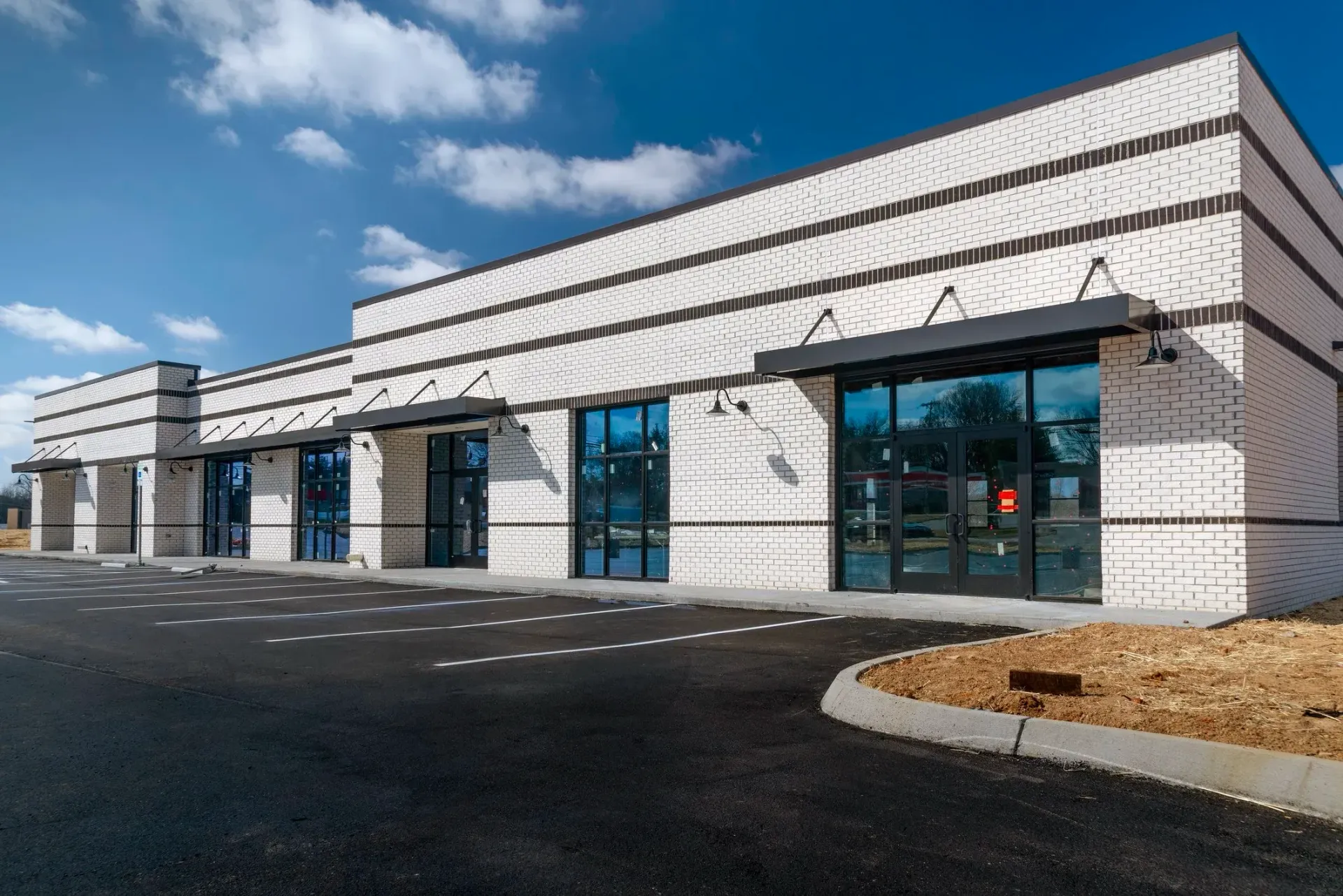 Modern commercial building with white brick facade, black awnings, and large glass windows.