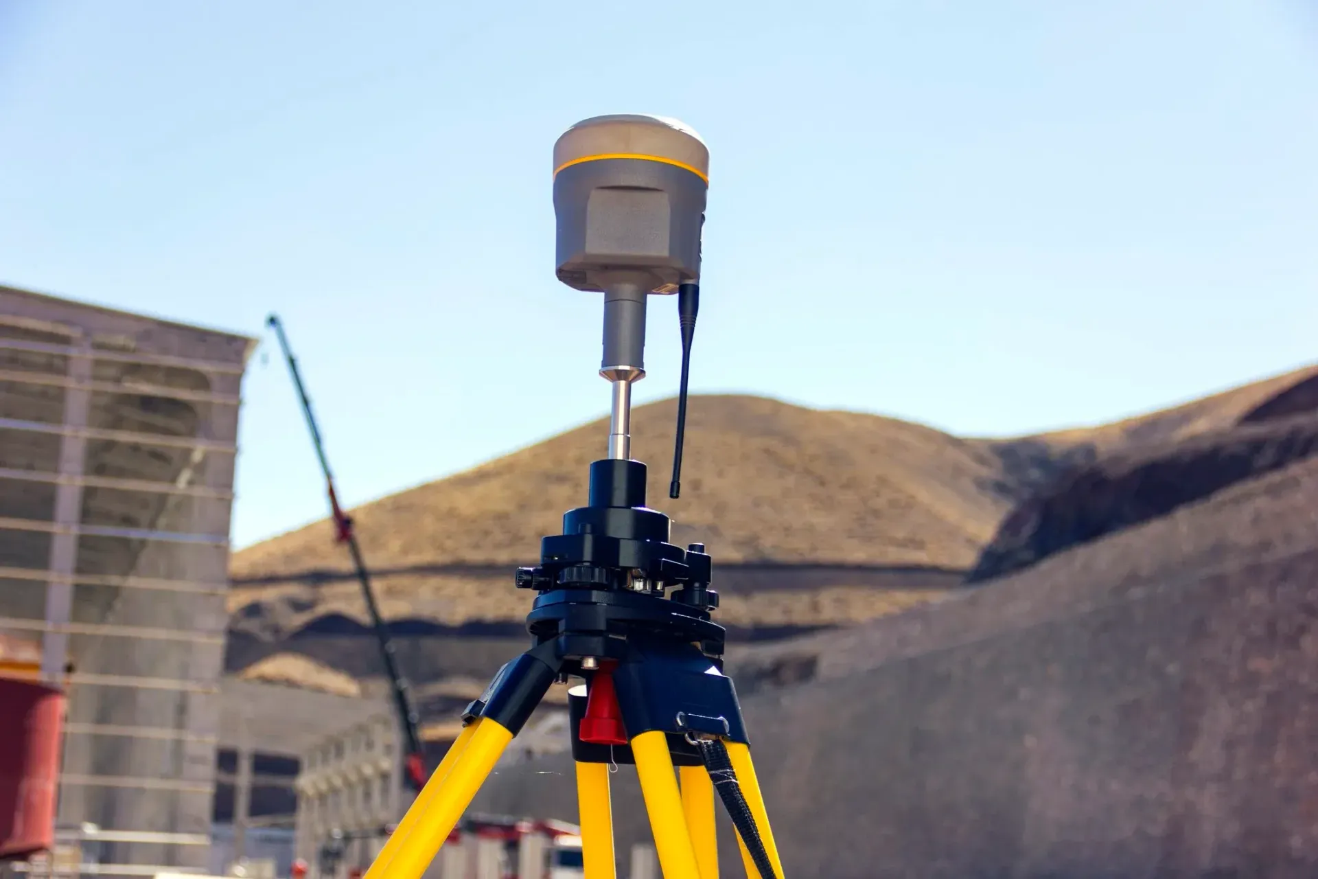 GPS receiver on a yellow-legged tripod, outdoors with a mountain in the background on a sunny day.