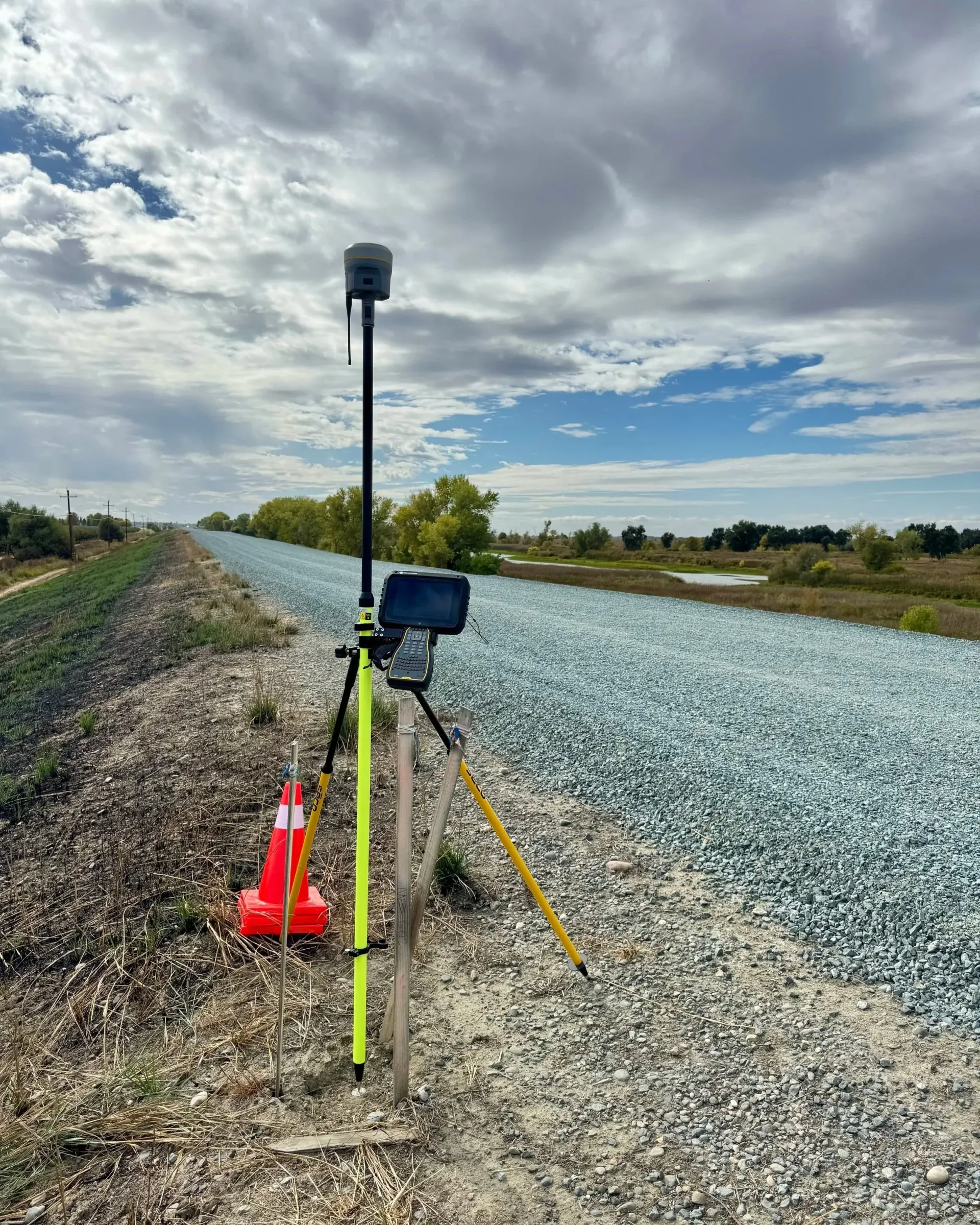 Surveying equipment set up on a gravel-covered embankment under a cloudy sky.