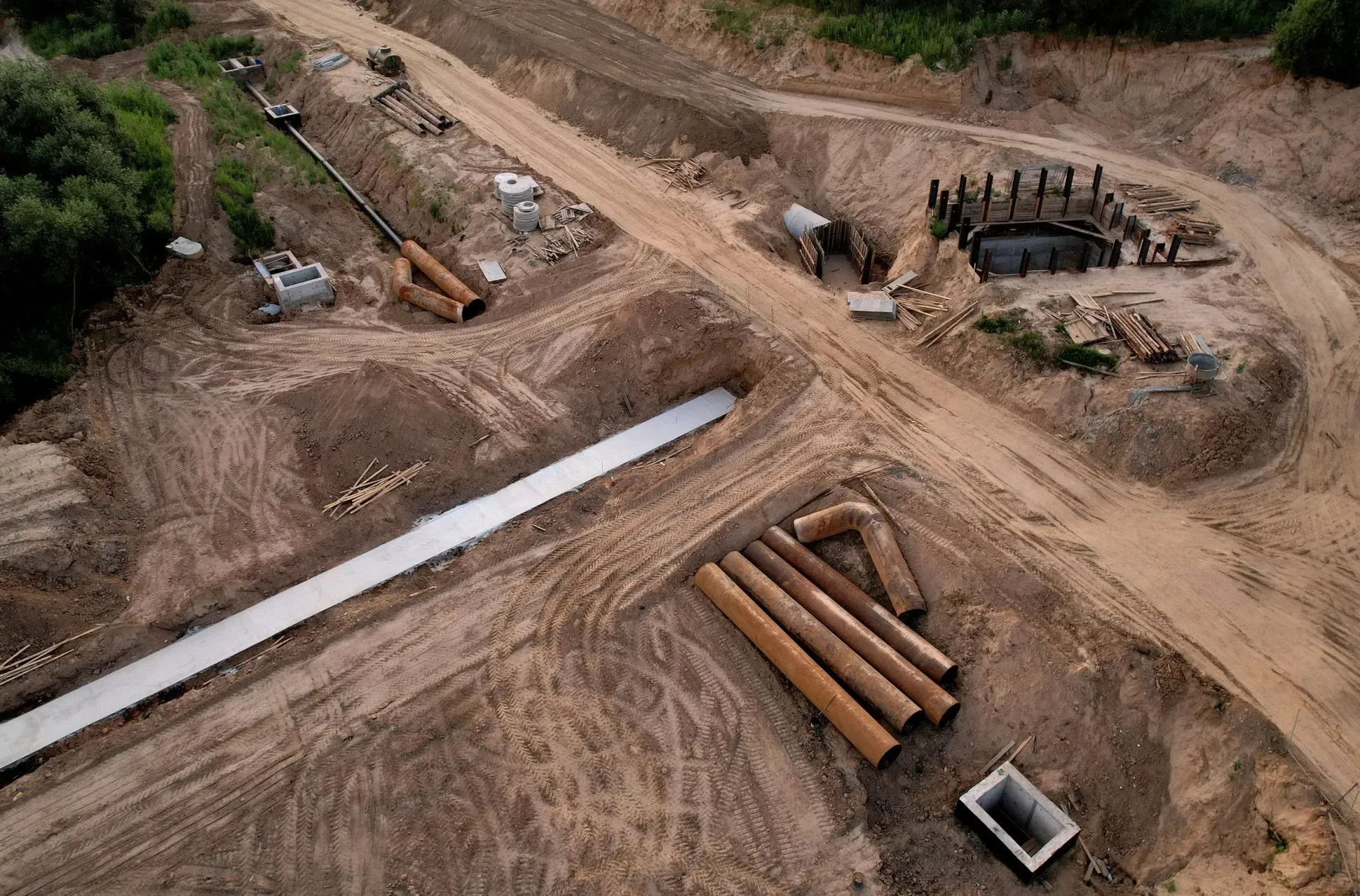 Aerial view of a construction site with trenches, pipes, and a concrete structure. Brown earth, beige pipes.