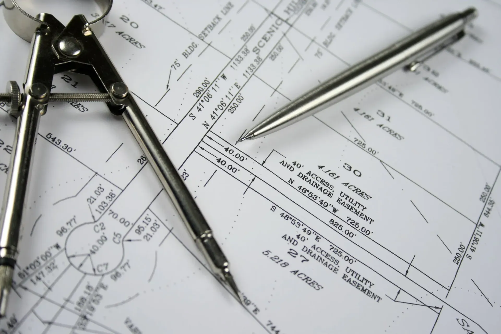 A surveyor's compass and pen on a detailed land survey map.