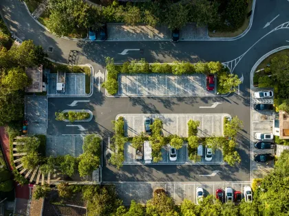 Overhead view of a parking lot surrounded by trees, with cars parked in designated spaces.