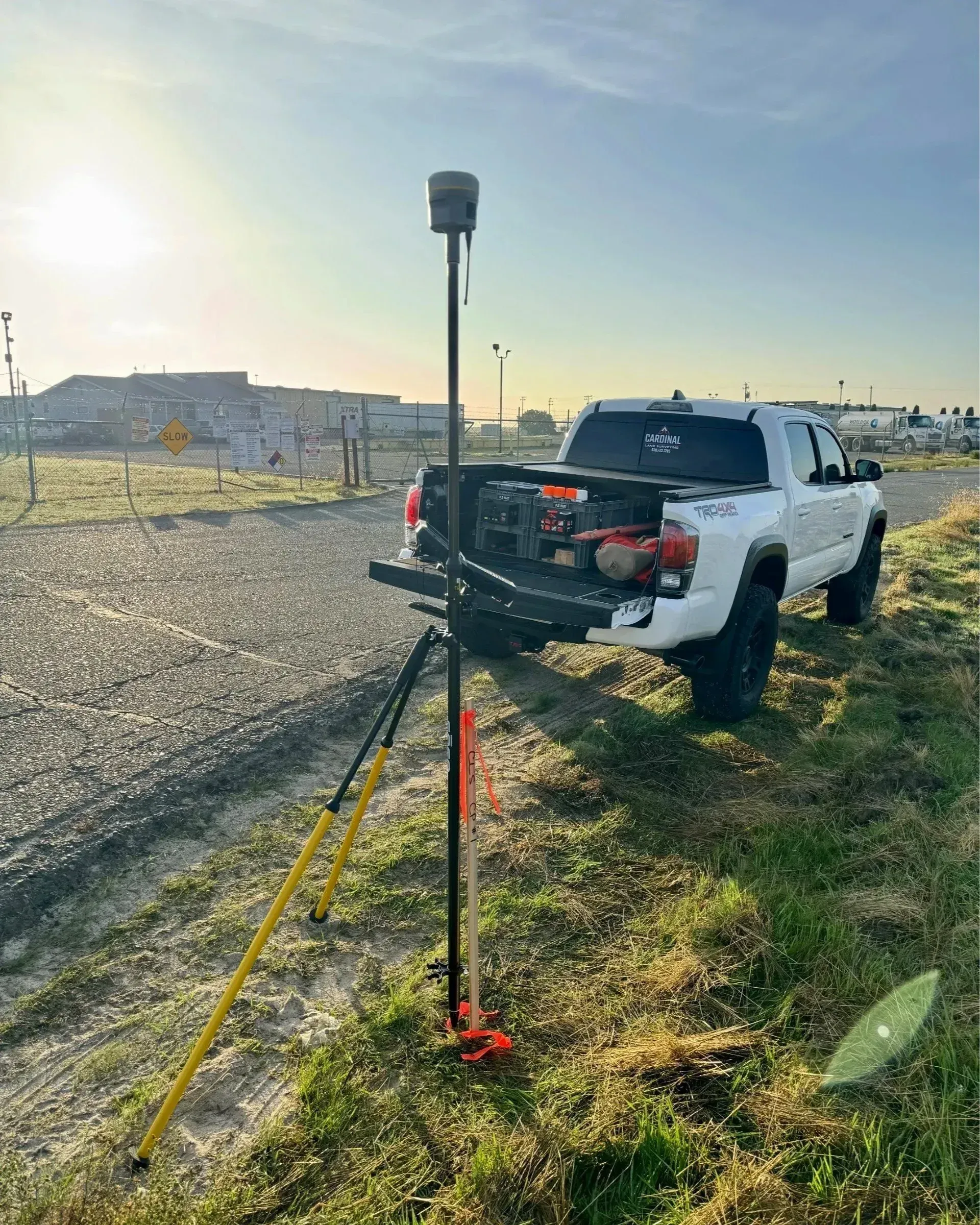 Surveying equipment set up near a white pickup truck. The sun shines brightly in the background.