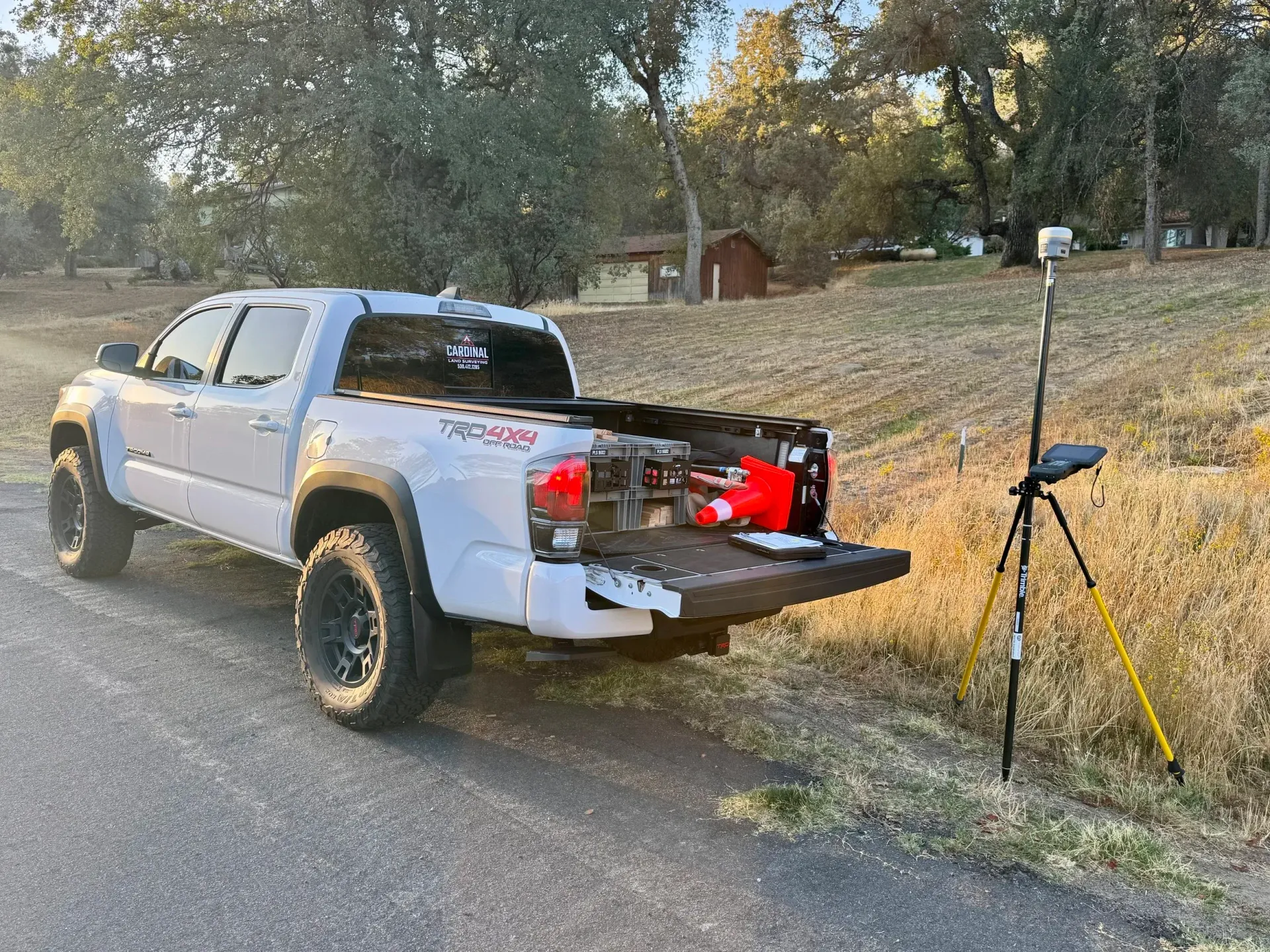 White pickup truck with open tailgate; tripod with equipment next to it, rural setting.