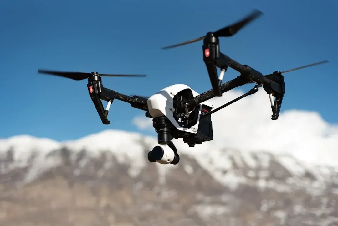 Drone flying with snowy mountains in the background, blue sky.