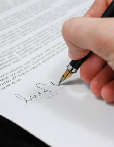 A hand signs a document with a black pen on white paper.