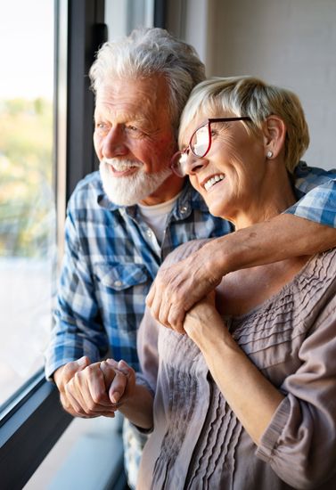 Two smiling people in plaid shirts leaning together by a window, looking outside