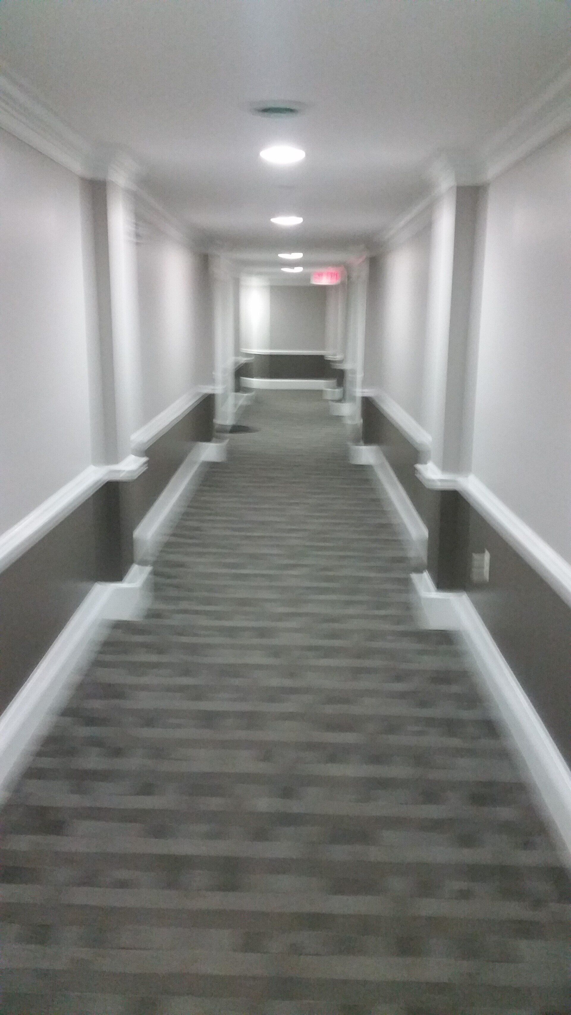 A long hallway with stairs and a red exit sign.