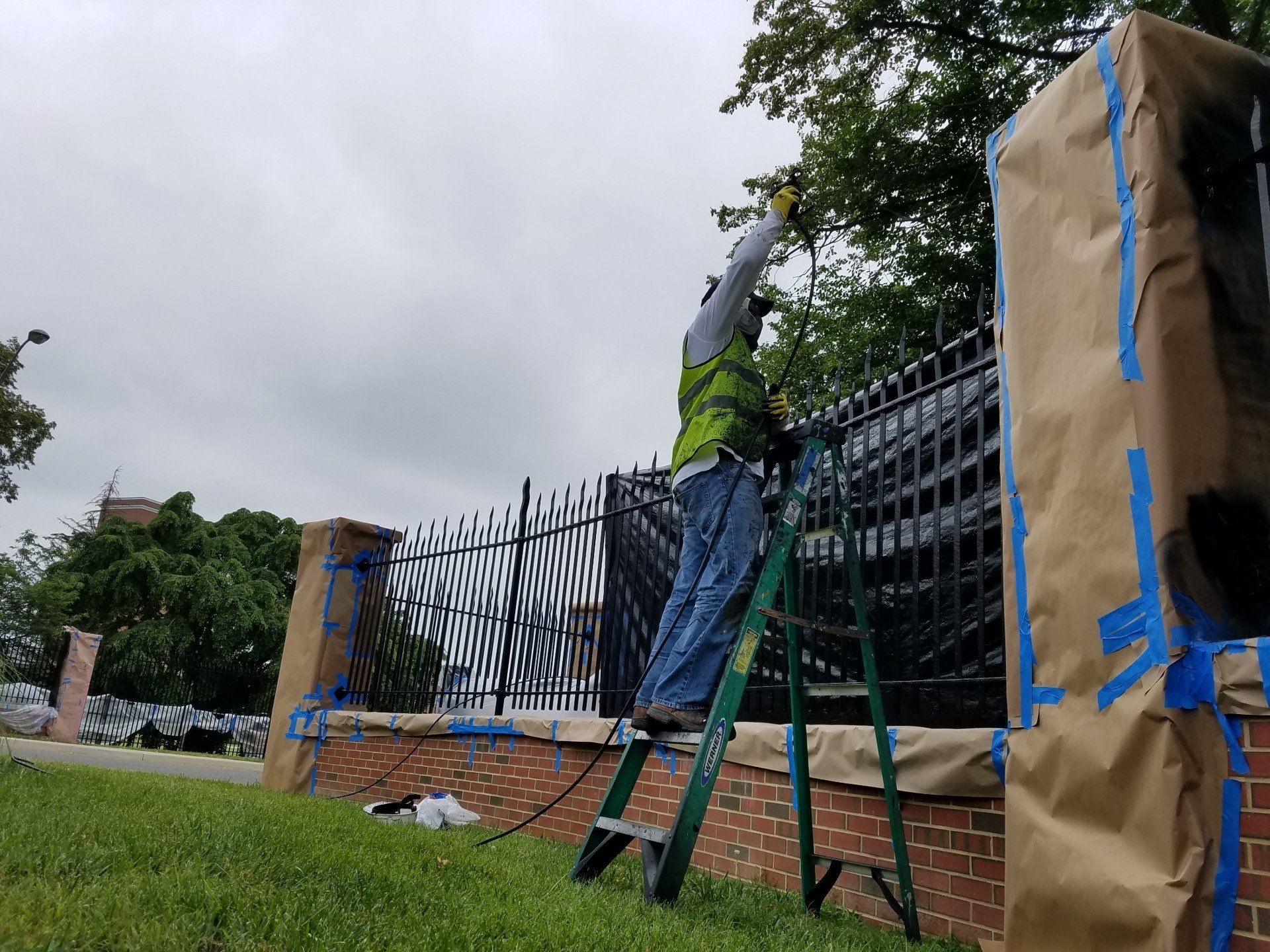 A man is standing on a ladder painting a fence.
