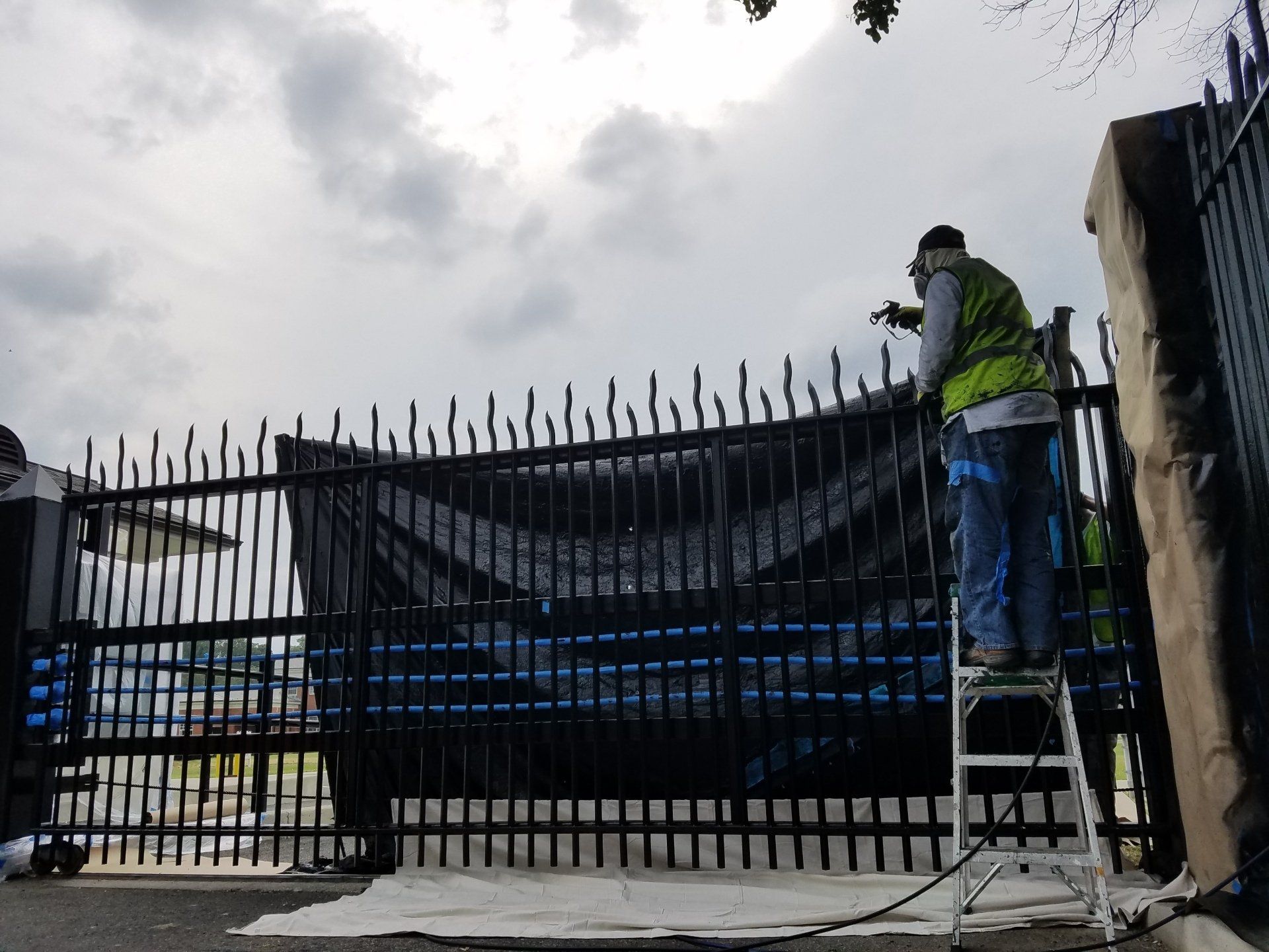 A man is standing on a ladder painting a gate.