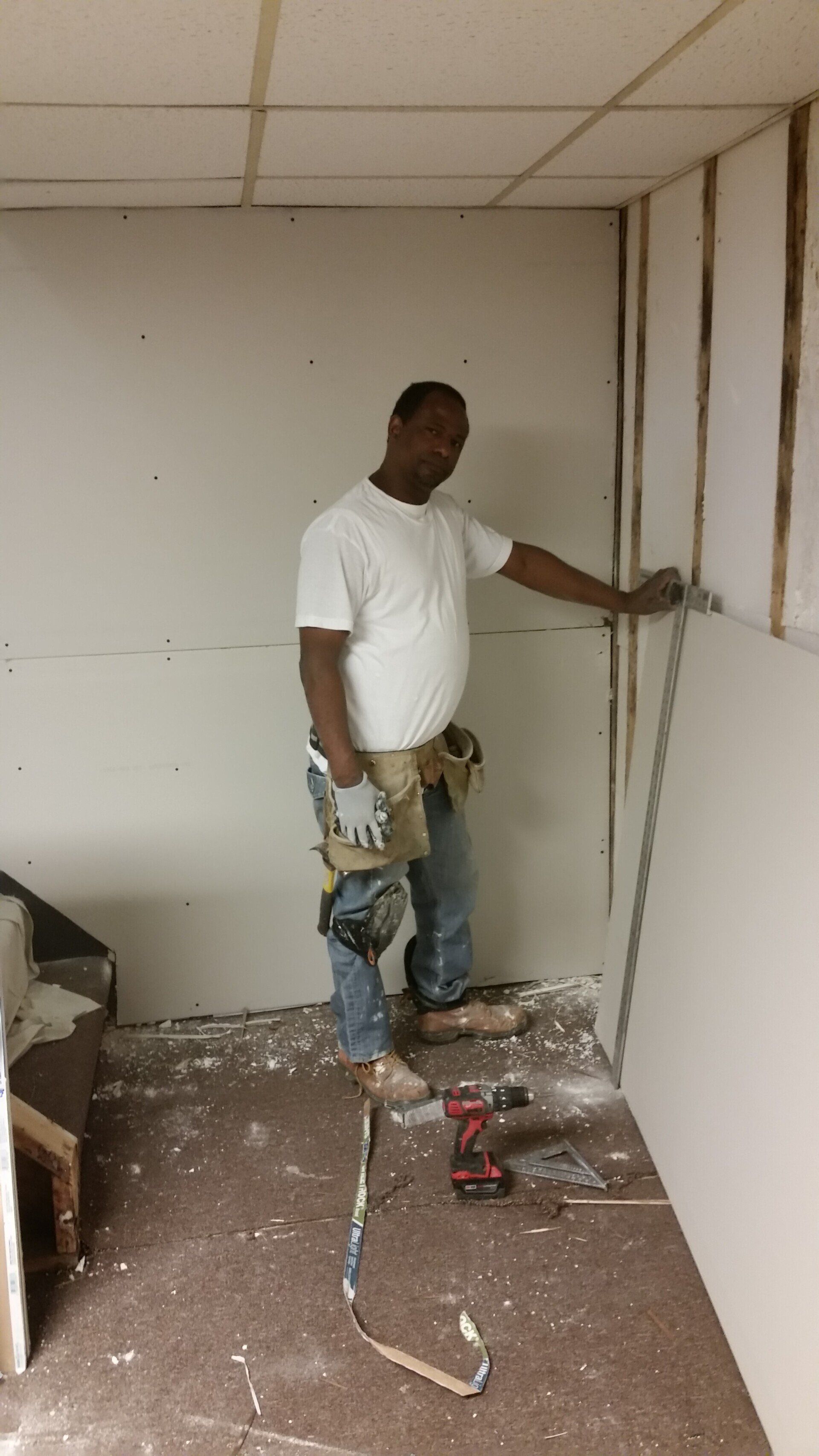 A man is standing in a room measuring a wall with a tape measure.