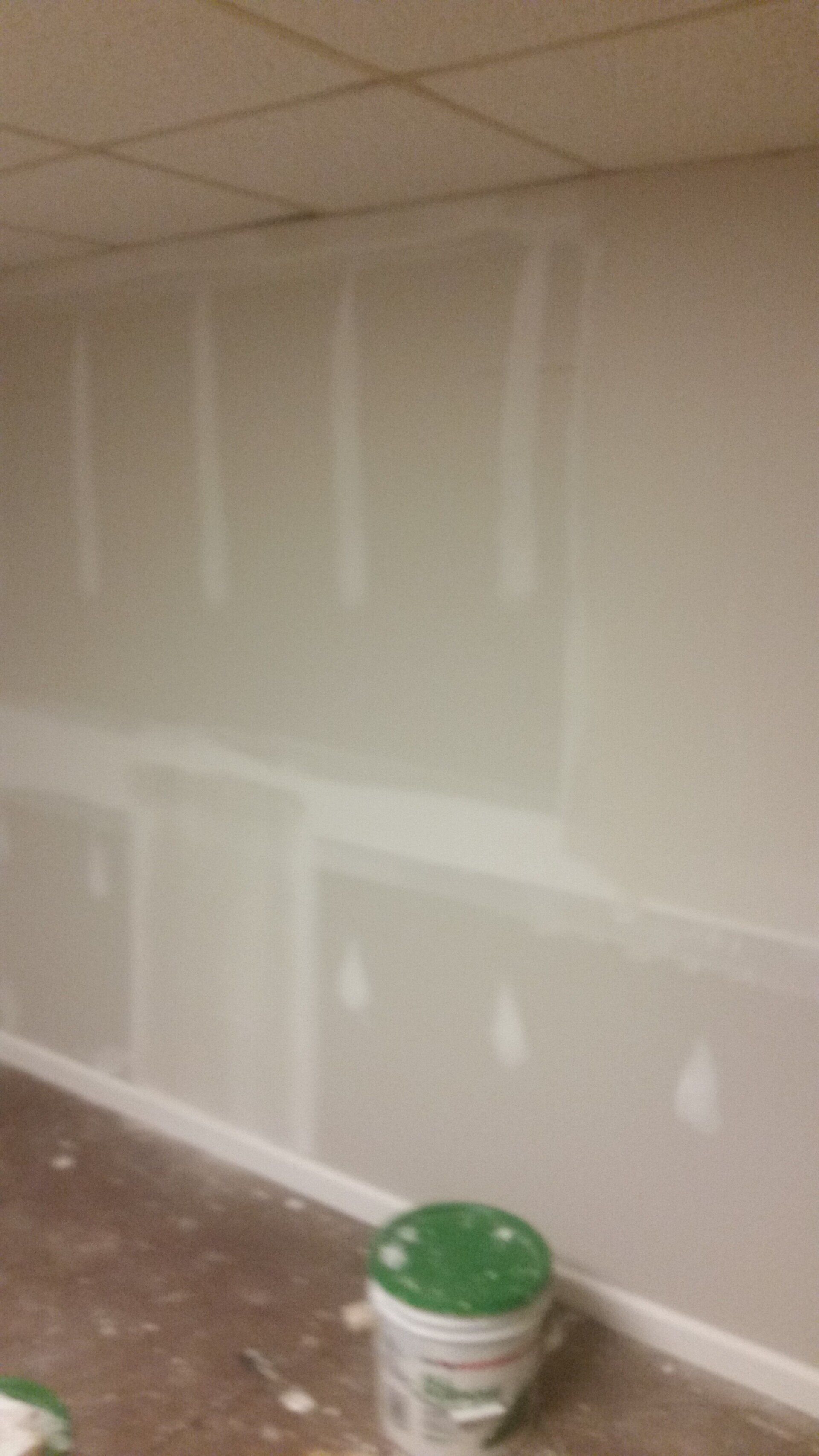 A bucket of paint is sitting on the floor in front of a wall.