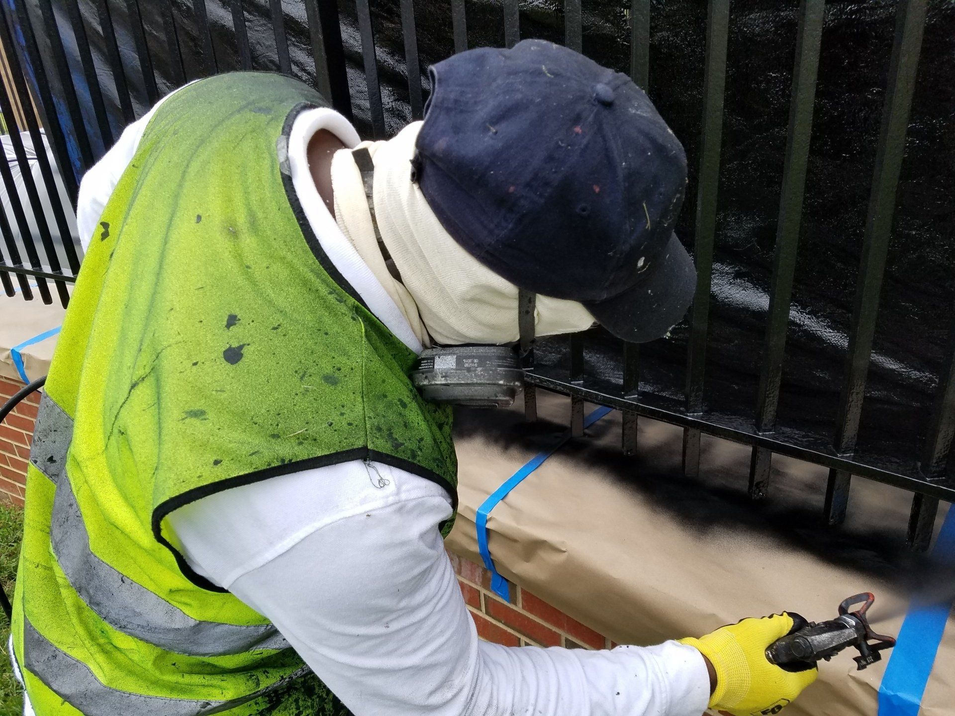 A man in a yellow vest is painting a fence