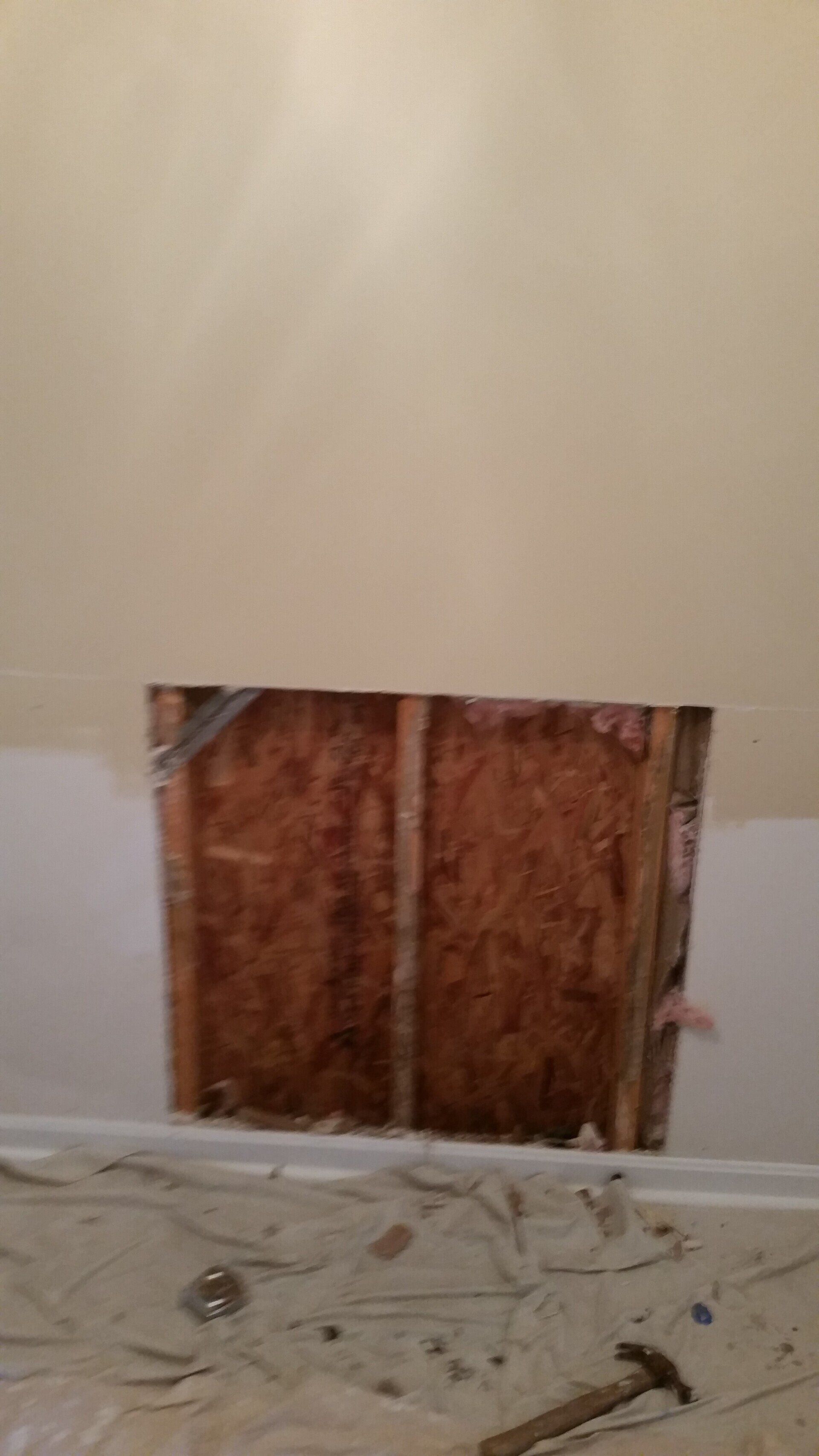 A hole in a wall in a room with a hammer on the floor.