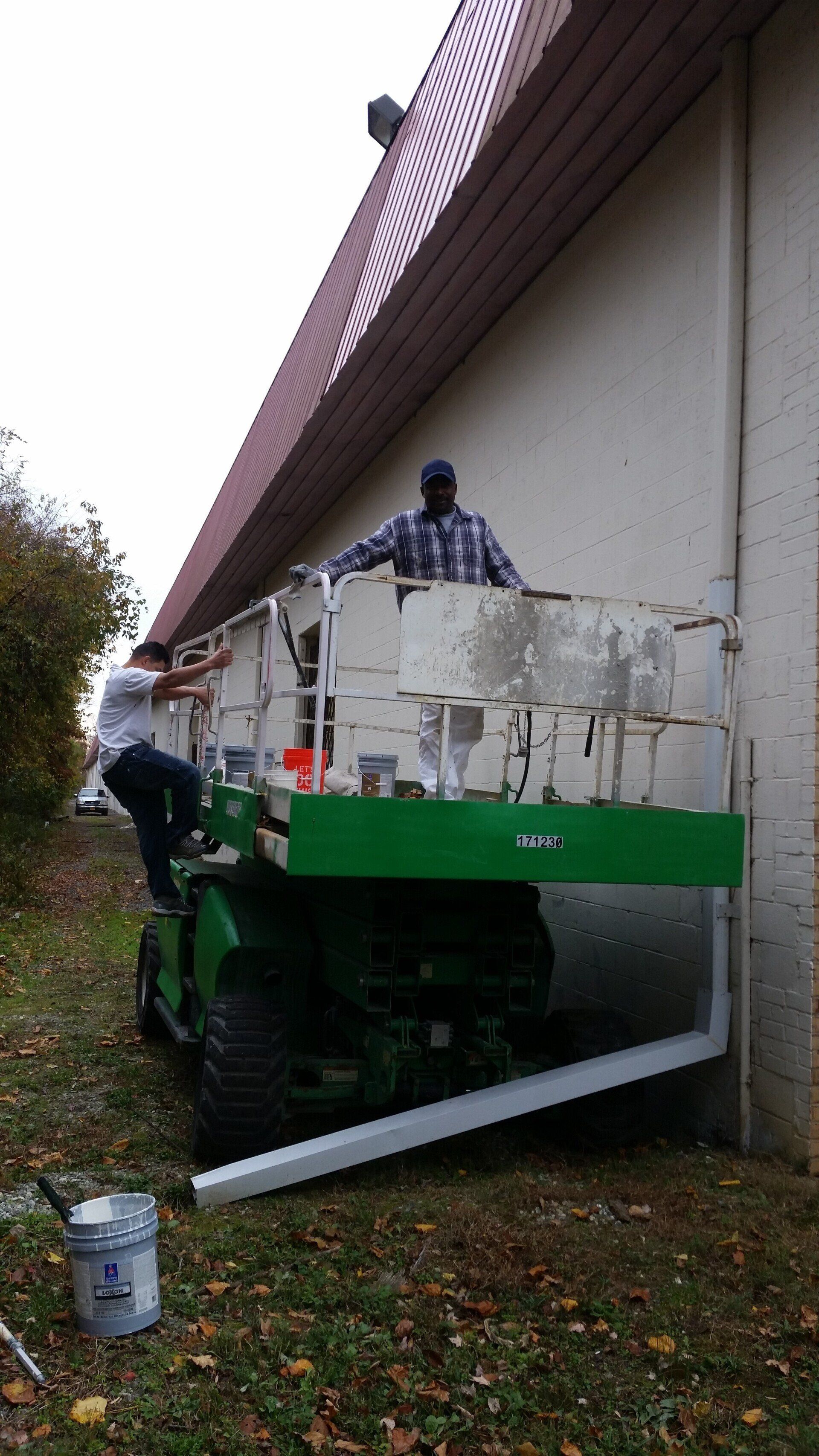 Two men are painting a building with a green lift.