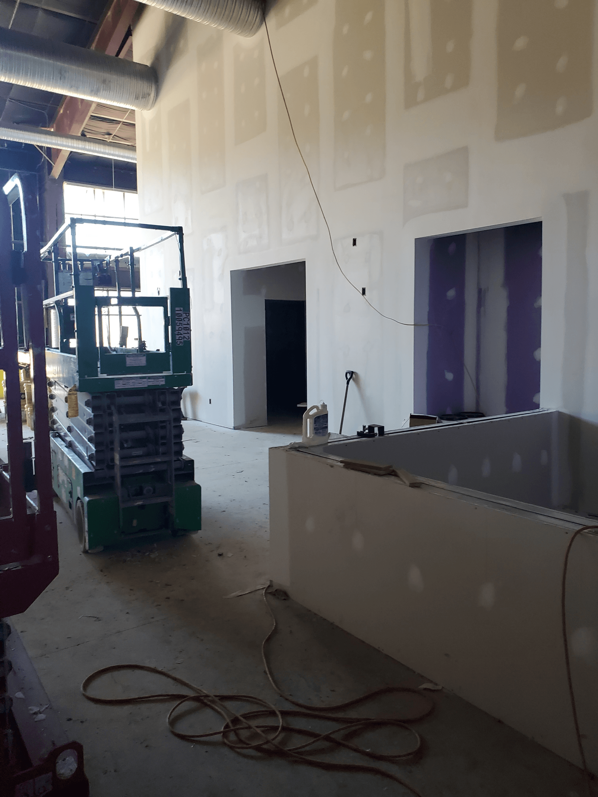 A green scissor lift is parked in a building under construction